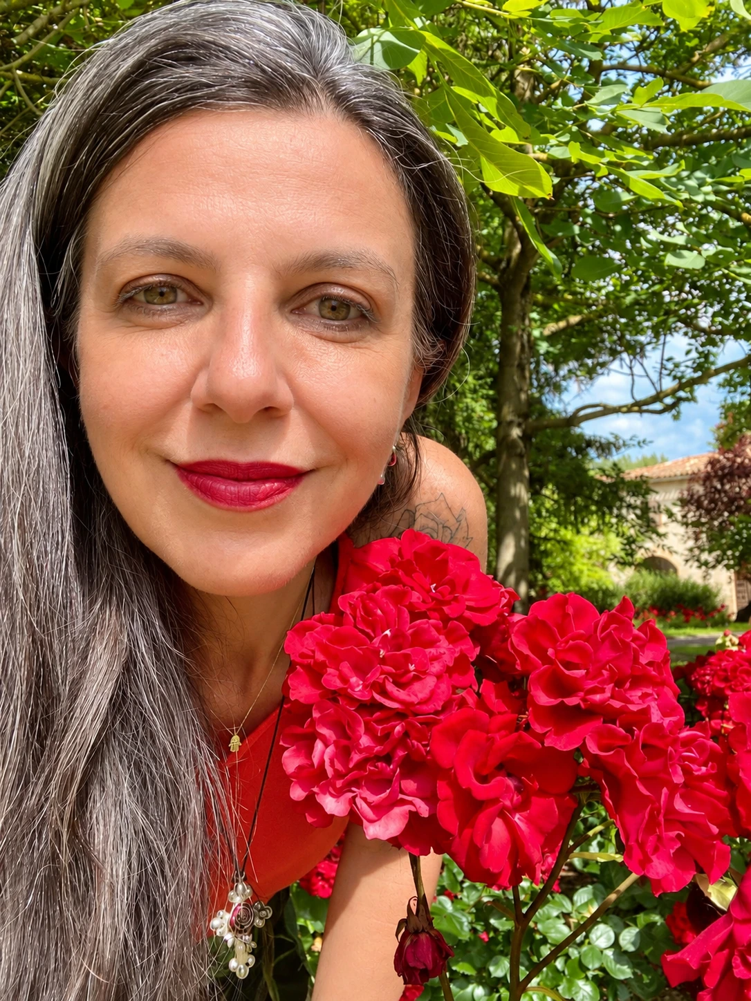 Adriana junto a rosas vermelhas, em um jardim.