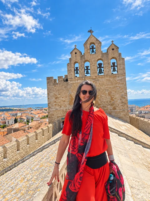Adriana de vermelho sobre uma muralha, com uma igreja ao fundo.