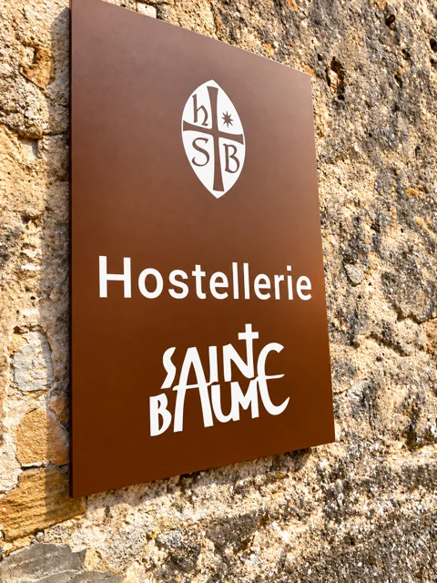 Placa da Hostellerie de la Sainte-Baume sobre uma parede de pedra.