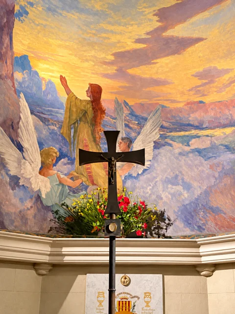 Cruz diante de uma pintura religiosa em tons dourados.